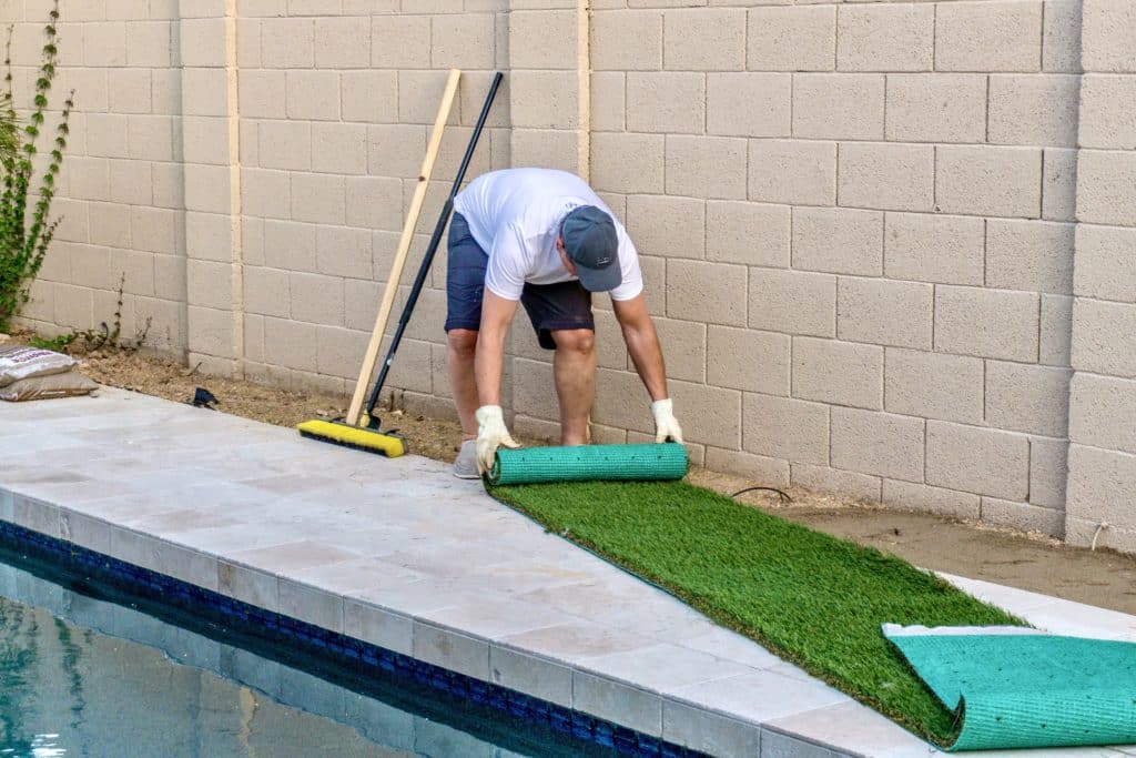 Man installing artificial turf by poolside.