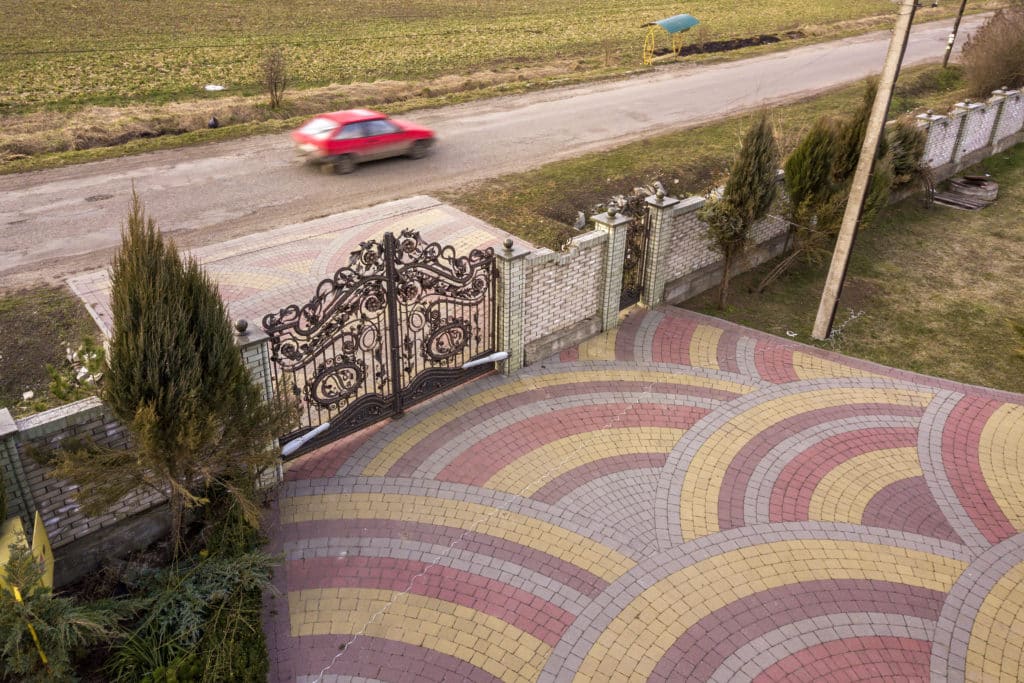 Ornate gate, patterned driveway, blurred car passing by.