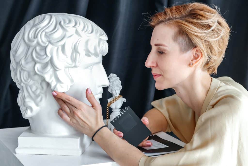 Woman examining classical bust sculpture with a magnifying glass.