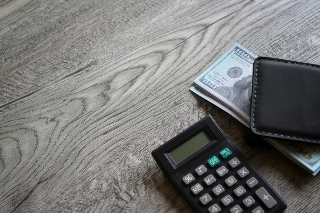 Calculator, money, and wallet on wooden surface.