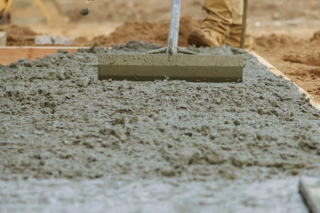 Worker smoothing wet concrete with trowel.