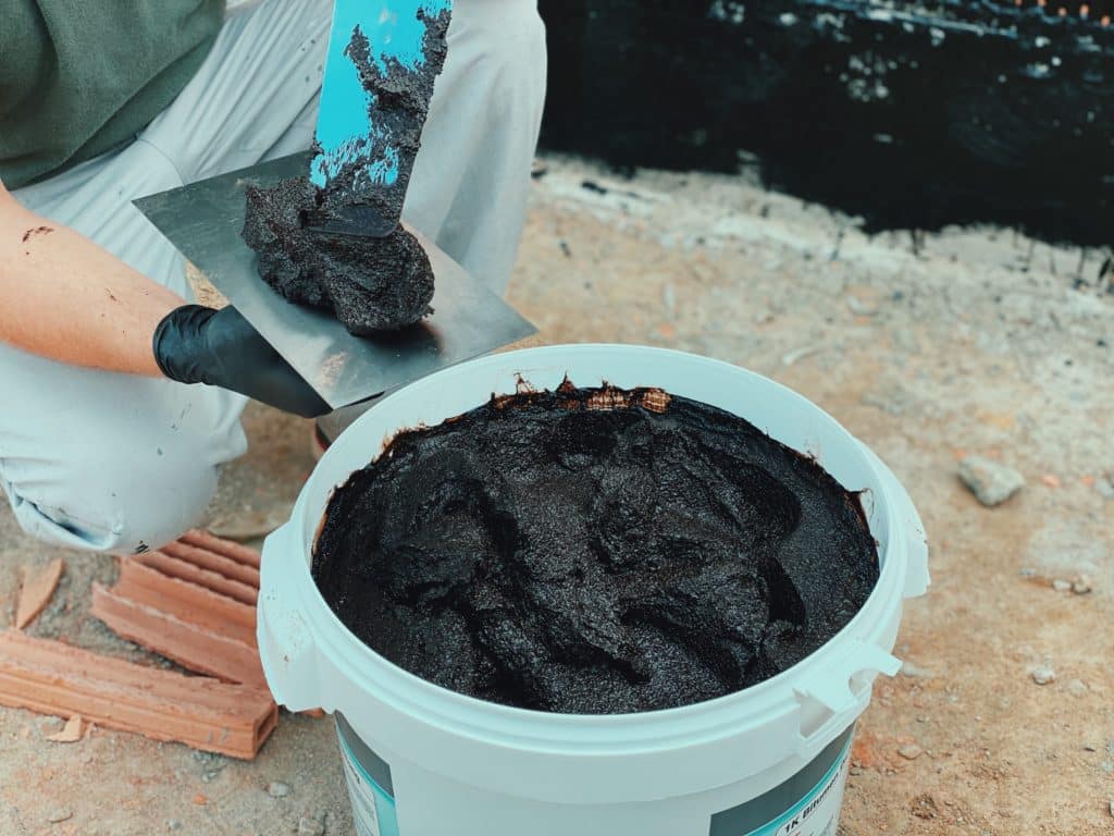 Person scooping black tar from bucket.