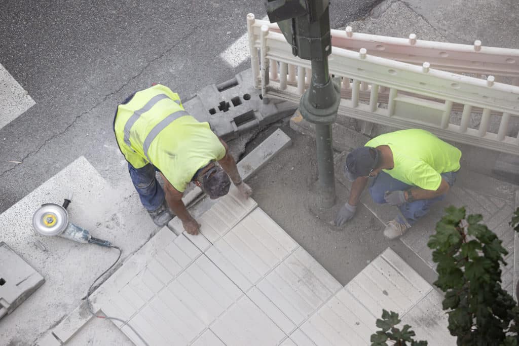 Workers laying sidewalk tiles near street.