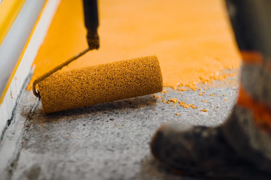 Paint roller applying orange paint on wall.