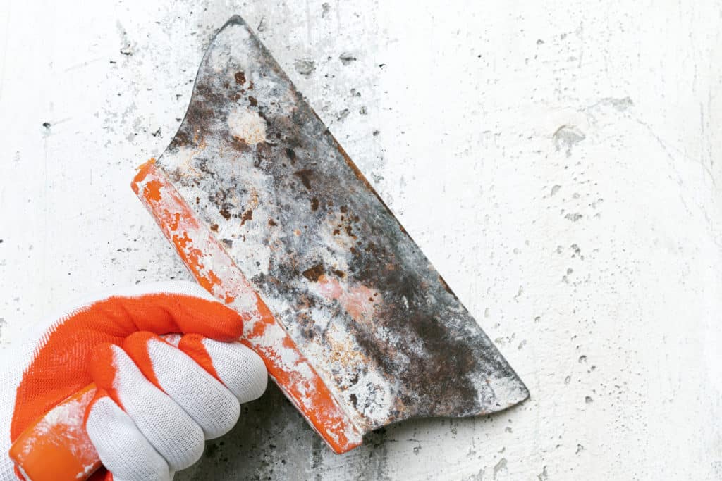 Hand holding a rusty putty knife on concrete.