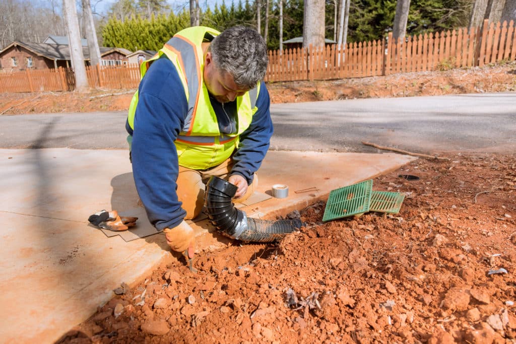 Worker installing drainage pipe on roadside.