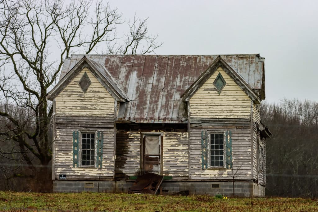 Dilapidated old house with peeling paint and bare trees.