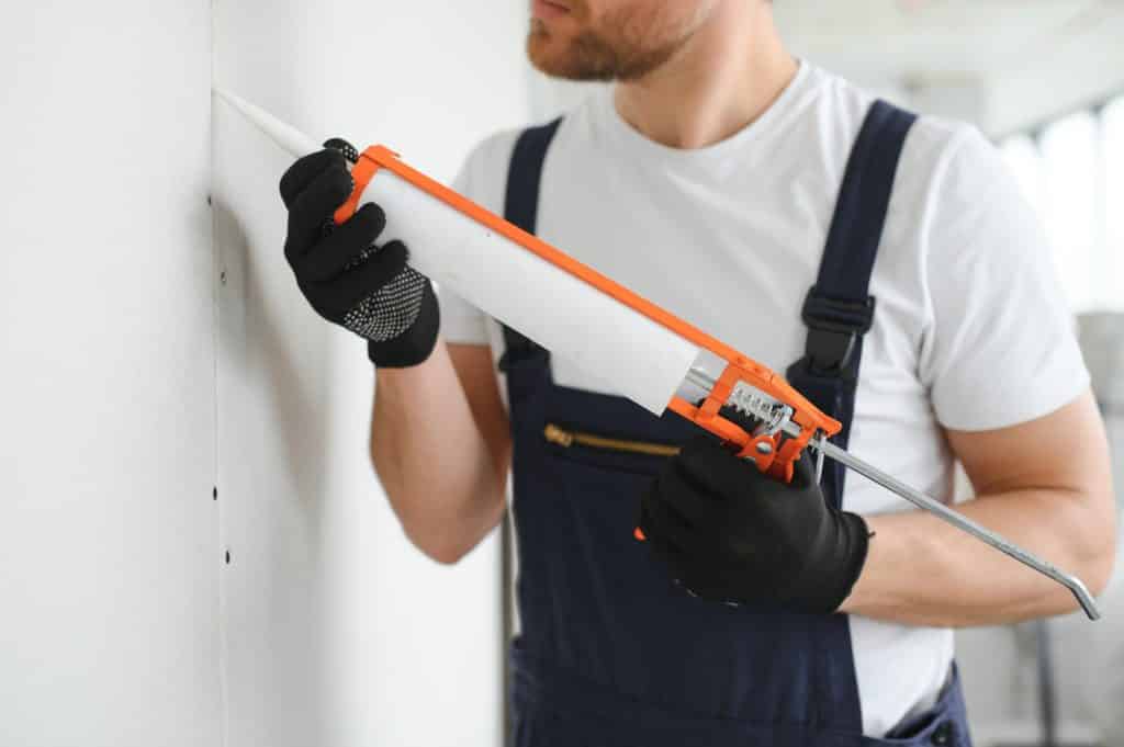 Worker applying caulk to seal wall.