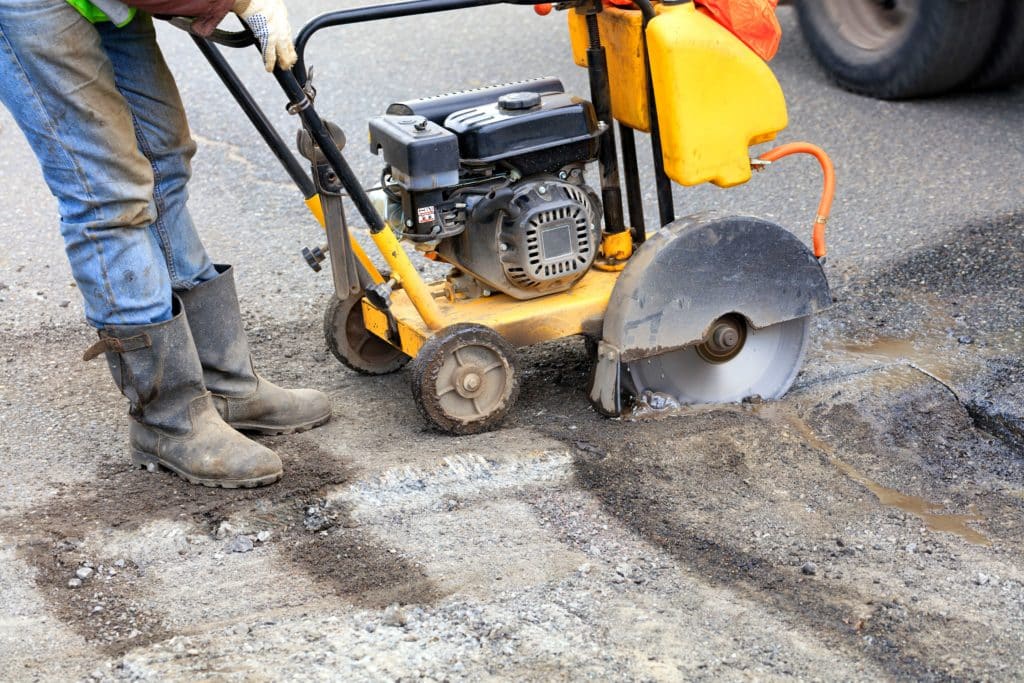 Worker cutting asphalt with road saw.