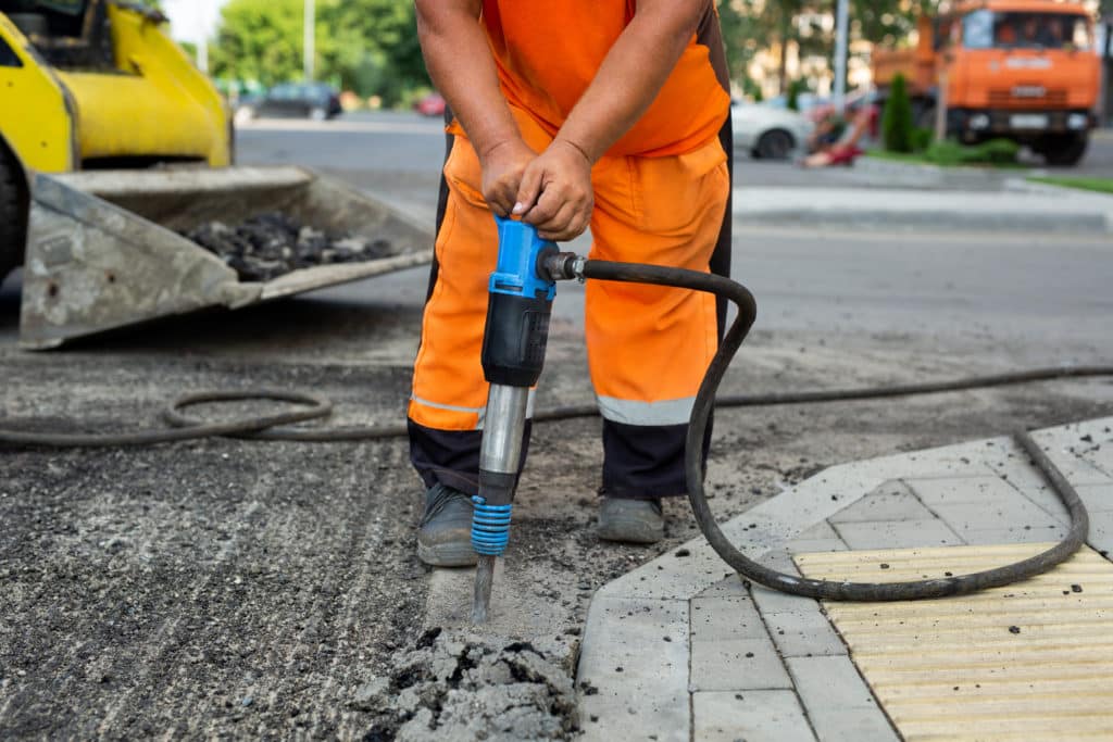 Worker using jackhammer on pavement.