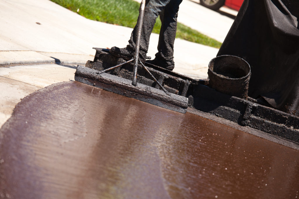 Worker applying hot tar for pavement repair.