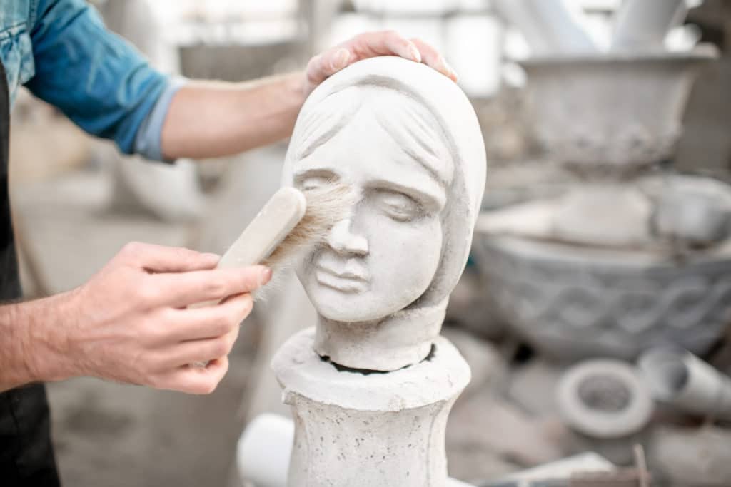 Sculptor brushing dust off stone statue's face.