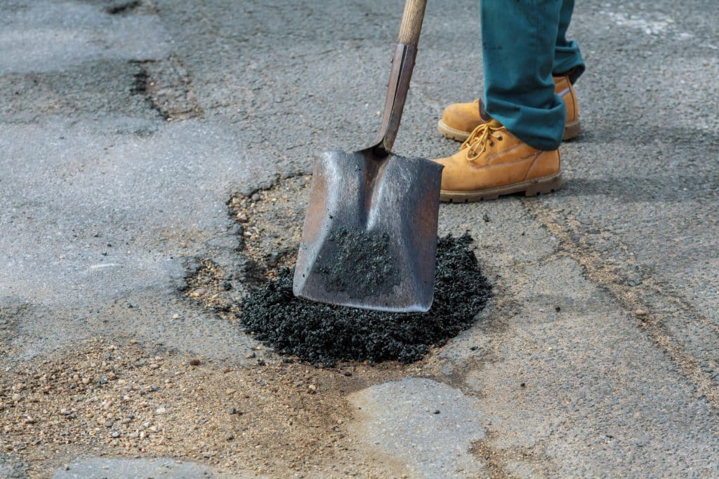 Worker repairing pothole with asphalt and shovel.