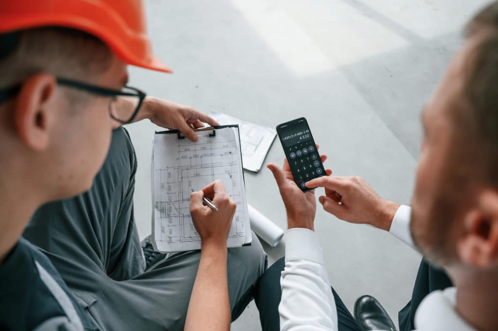 Two engineers discussing blueprints with calculator.