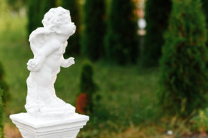 White cherub statue in garden setting.