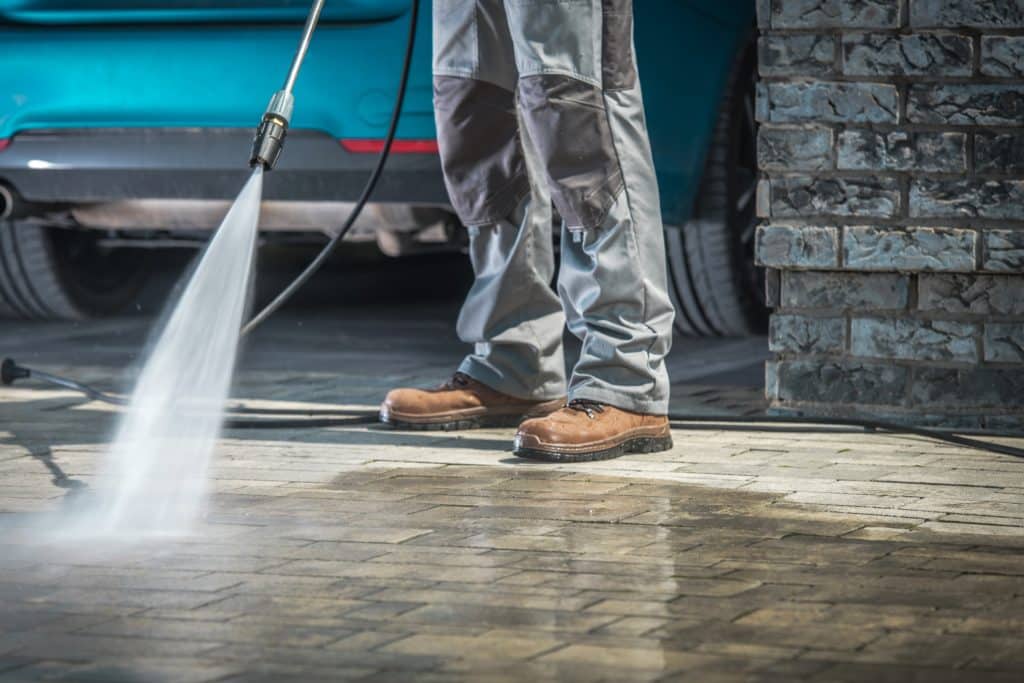 Pressure washing driveway near blue car.