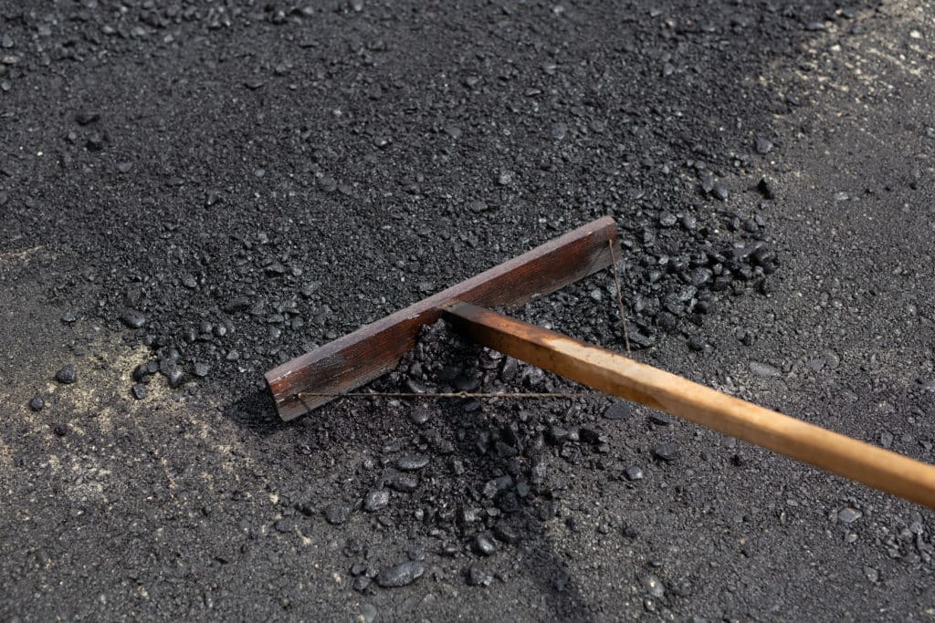 Rake on fresh asphalt road construction site.