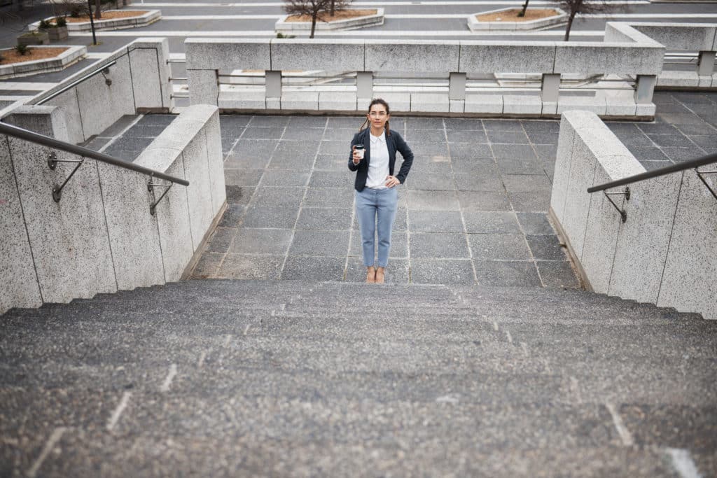 Woman holding coffee on outdoor stairs.