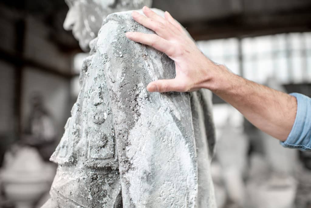 Hand sculpting a stone statue in workshop.