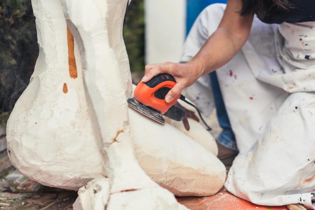 Sculptor sanding a statue with orbital sander.