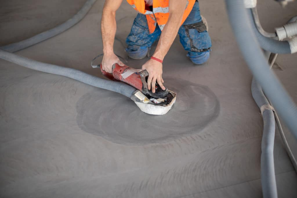 Worker sanding floor with handheld power tool.